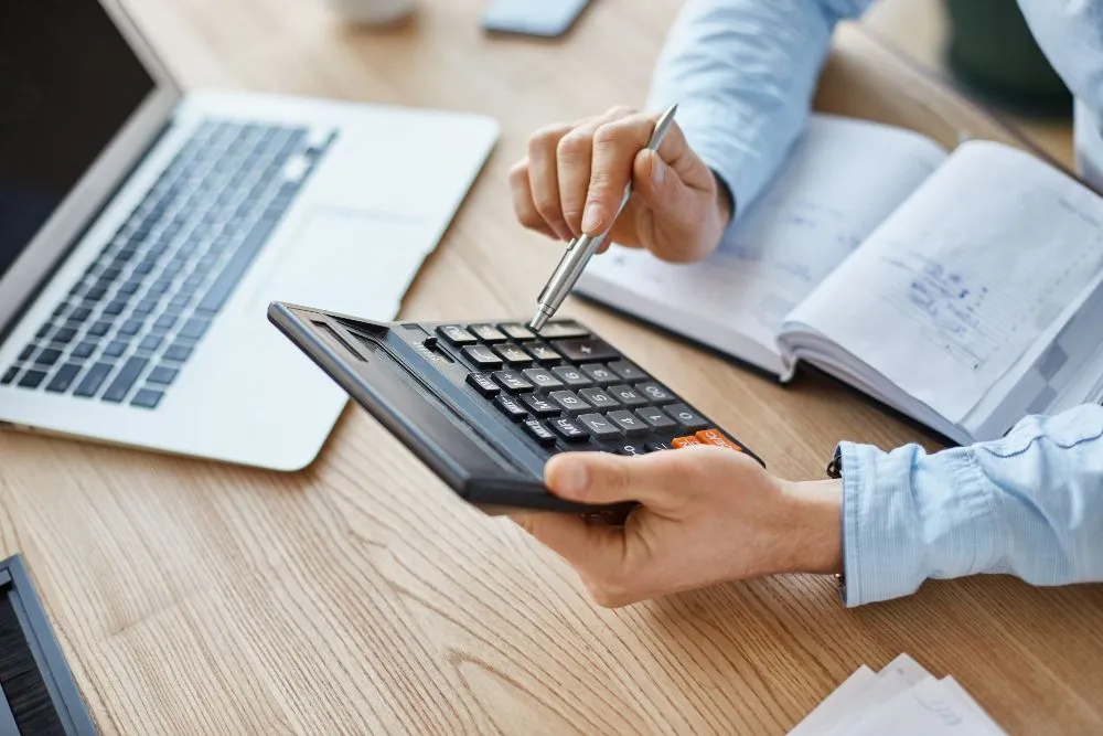 gestionnaire financier professionnel sérieux, tenant la calculatrice en mains, vérifiant les bénéfices du mois